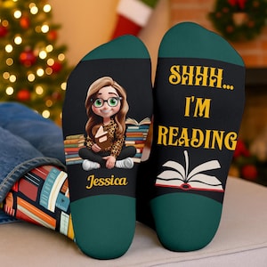 May include: Black socks with a green heel and toe. One sock features a cartoon girl with glasses holding a book, the name "Jessica", and a stack of books. The other sock says "SHHH... I'M READING" with an open book graphic.