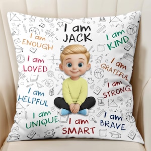 May include: White decorative pillow with a cartoon illustration of a boy named Jack. The pillow is decorated with the phrases "I am enough", "I am loved", "I am helpful", "I am unique", "I am kind", "I am grateful", "I am strong", "I am smart", and "I am brave".