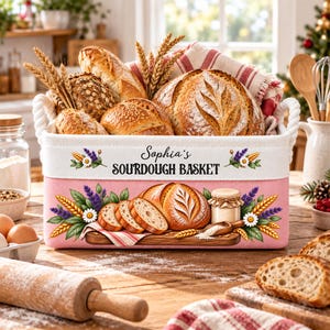 May include: A rectangular fabric storage basket with rope handles, featuring a pink base and white top band. The text reads Sophia's SOURDOUGH BASKET, accompanied by illustrations of wheat, lavender, daisies, and sliced bread on a wooden board.