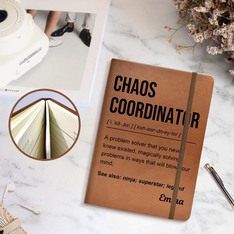 May include: A brown notebook with the words "CHAOS COORDINATOR" printed in black. The notebook has a brown elastic band and contains lined pages. The text below the title defines the term and includes the name "Ema".