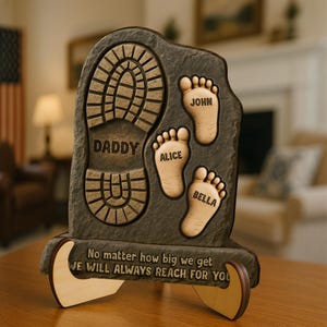 May include: A brown wooden plaque with a footprint design. The plaque has the words "Daddy", "Alice", "John", and "Bella" inscribed on it. The plaque also has the text "No matter how big we get, we will always reach for you".