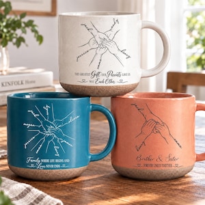 Peut inclure: Trois tasses en céramique crème, bleu sarcelle et corail, avec une finition mouchetée et une base aspect liège. Elles présentent un dessin au trait de mains jointes avec des prénoms et les textes "The greatest gift our parents gave us was each other", "Family where life begins and love never ends" et "Brother & Sister forever linked together".