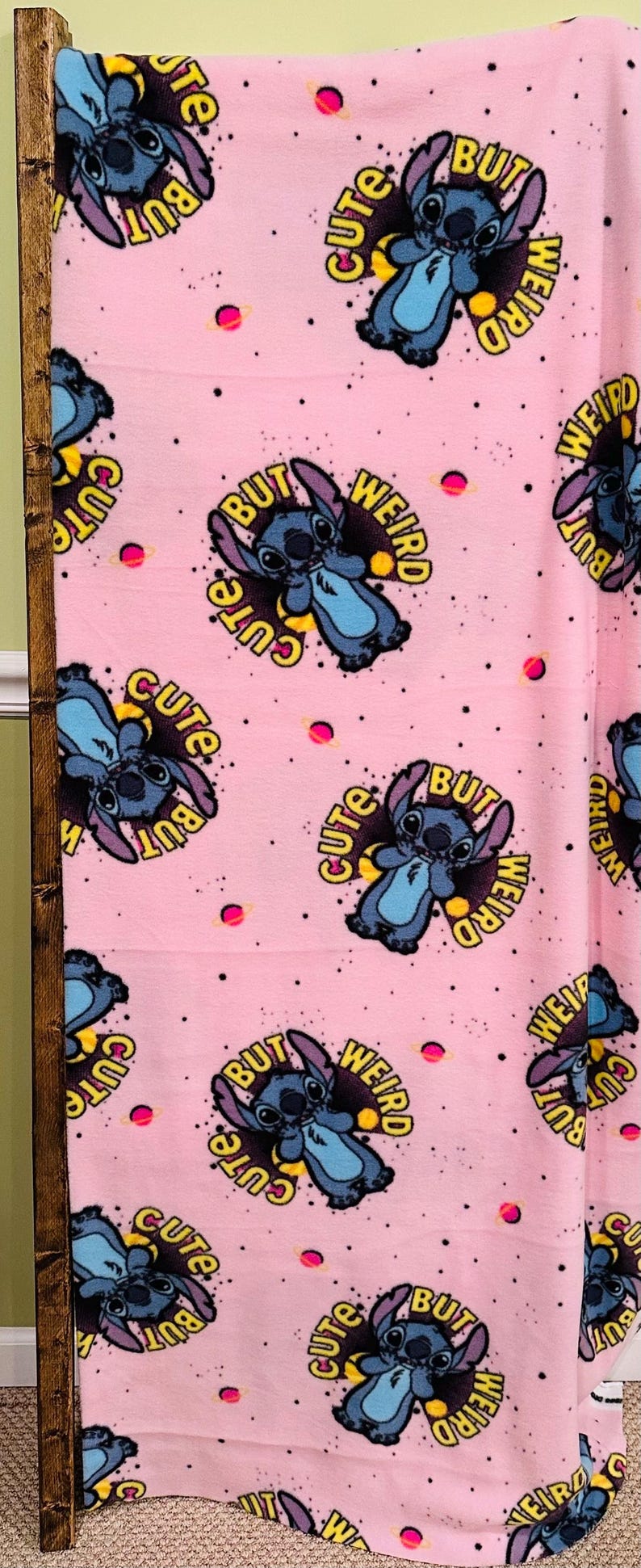 Pu&ograve; includere: Coperta in pile rosa con un motivo ripetuto del personaggio Stitch di Lilo & Stitch. Ogni Stitch &egrave; circondato dalle parole "Cute But Weird", con piccoli pianeti rosa sparsi sullo sfondo.