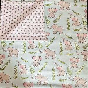 May include: A baby blanket with a light blue background featuring a repeating pattern of pink elephants and green leaves. One side of the blanket is a light pink fabric with gray polka dots.