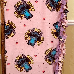 Pu&ograve; includere: Coperta in pile rosa con un motivo ripetuto di un personaggio dei cartoni animati e la scritta "Cute But Weird". La coperta ha un bordo sfrangiato nei toni del viola e del rosa. Un plaid accogliente.