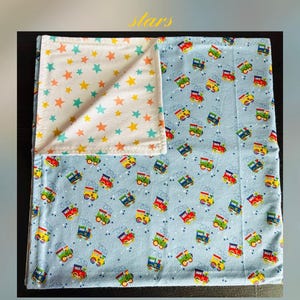 May include: A baby blanket with a light blue background featuring colorful cartoon trains. The reverse side displays a white fabric with orange, yellow, and teal stars. The blanket has the text "Choo choo train & stars" and "Cozy dozy".