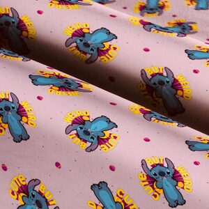 Pu&ograve; includere: Tessuto rosa chiaro con un motivo ripetuto del personaggio Stitch di Lilo & Stitch. Ogni illustrazione di Stitch &egrave; blu con un'esplosione gialla e viola, e le parole "BUT CUTE WEIRD" sono stampate attorno al personaggio. Piccoli punti rosa sparsi.