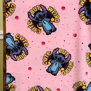 Pu&ograve; includere: Coperta rosa con un motivo ripetuto di un personaggio dei cartoni animati blu con le parole "Cute" e "Weird". Il design include pianeti rosa e punti neri.