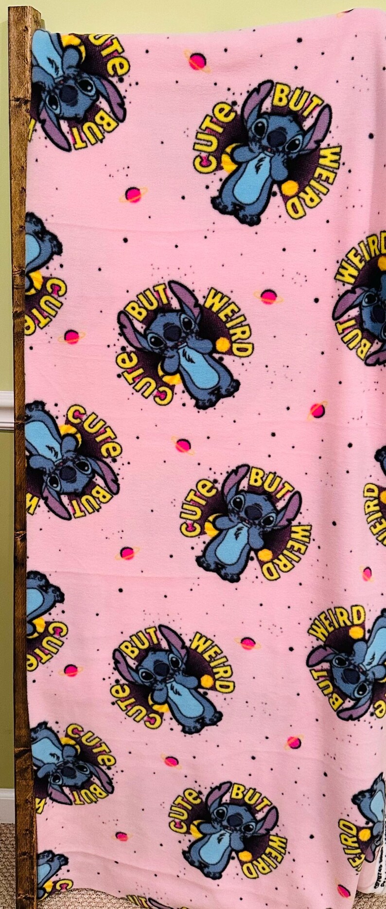 Pu&ograve; includere: Coperta rosa con un motivo ripetuto di un personaggio dei cartoni animati blu con le parole "Cute" e "Weird". Il design include pianeti rosa e punti neri.