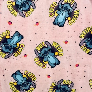 Pu&ograve; includere: Tessuto rosa chiaro con un motivo ripetuto di un personaggio alieno blu con grandi orecchie. Ogni personaggio &egrave; circondato da un cerchio giallo con le parole "Cute But Weird". Piccoli pianeti e stelle sono sparsi sullo sfondo.