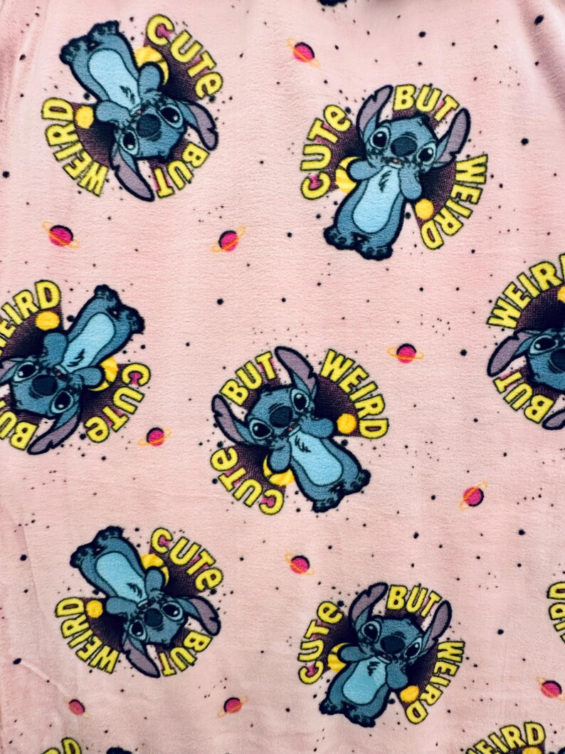 Pu&ograve; includere: Tessuto rosa chiaro con un motivo ripetuto di un personaggio alieno blu con grandi orecchie. Ogni personaggio &egrave; circondato da un cerchio giallo con le parole "Cute But Weird". Piccoli pianeti e stelle sono sparsi sullo sfondo.