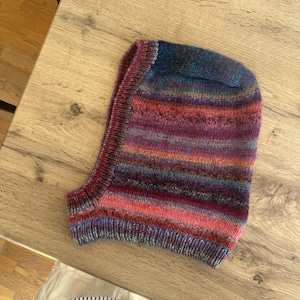 May include: A striped knitted balaclava in shades of pink, purple, blue, and brown. The balaclava is made of a soft, warm yarn and has a long neck.