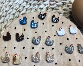 May include: A collection of ceramic chicken figurines in various colors and designs, displayed on a wooden board with holes. The figurines are arranged in a circular pattern, with the heads facing inwards.