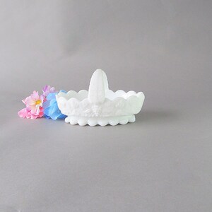 May include: White milk glass basket with a scalloped edge and a handle. The basket is decorated with a floral design.
