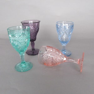 May include: Four vintage glass goblets in different colors: teal, purple, light blue, and pink. The goblets have a decorative, embossed pattern.