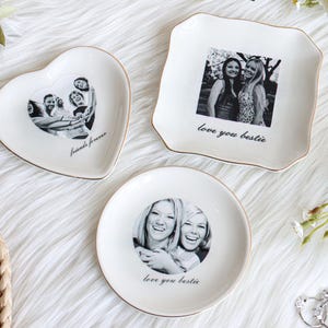 May include: Three white ceramic trinket dishes with gold rims. One is heart-shaped with a photo and the text "friends forever." Another is square with a photo and the text "love you bestie." The third is round with a photo and the text "love you bestie."
