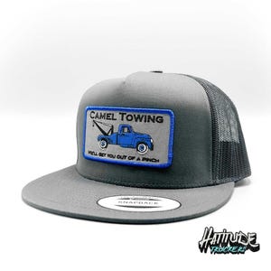 May include: Gray and black trucker hat with a blue and white patch that says "Camel Towing" and features a cartoon tow truck. The patch also says "We'll get you out of a pinch".