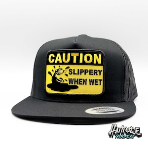 Puede incluir: Gorra de camionero negra con un parche de señal de advertencia amarillo y negro que dice "ATENCIÓN RESBALADIZO CUANDO ESTÁ MOJADO" y presenta una imagen de dibujos animados de una rata.