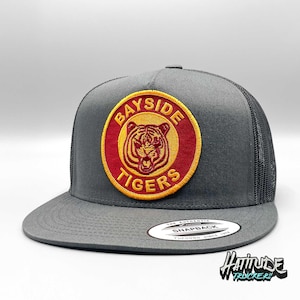 Może przedstawiać: Szara i czarna czapka trucker z naszywką wyszywaną na czerwono i żółto z napisem "Bayside Tigers" i wizerunkiem głowy tygrysa.