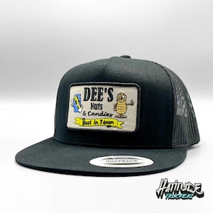 May include: Black trucker hat with a black mesh back. The hat has a square patch on the front that says "Dee's Nuts & Candies Best in Town" with a cartoon peanut and a can of soda.