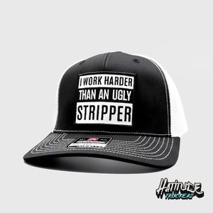 Puede incluir: Gorra de camionero negra y blanca con el texto "I WORK HARDER THAN AN UGLY STRIPPER" en un parche cuadrado. La gorra tiene una parte trasera de malla blanca y una visera curva con costuras blancas. La marca "Hattitude Truckers" es visible.
