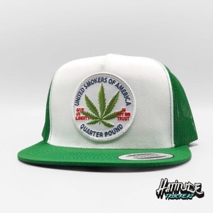 Könnte beinhalten: Weiße und grüne Trucker-Kappe mit einem gestickten Patch aus grünem Marihuana-Blatt, auf dem "United Smokers of America Give Us Liberty In Pot We Trust Quarter Pound" steht.
