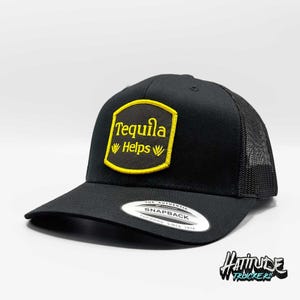Könnte beinhalten: Schwarze Trucker-Kappe mit einem gelben Patch, auf dem in einer Vintage-Schriftart "Tequila Helps" steht. Die Kappe hat ein schwarzes Netzrücken und einen Druckknopfverschluss.