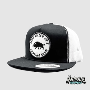 May include: Black and white trucker hat with a white mesh back. The front of the hat features a white circle patch with the text "Ain't Killed Shit Hunting Club" and a black silhouette of a wild boar.