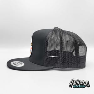 May include: Black trucker hat with a black mesh back and a white patch with colorful graphics. The patch says "Attitude Truckers".