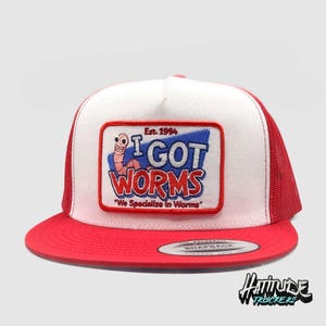 May include: A white and red trucker hat with a red mesh back. The front of the hat has a blue and red patch with a worm and the text "Est. 1994 I GOT WORMS "We Specialize in Worms".