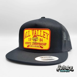 Peut inclure: Casquette de camionneur noire avec un patch jaune et rouge qui dit "All Valley Karate Championship 1984 Los Angeles, CA".