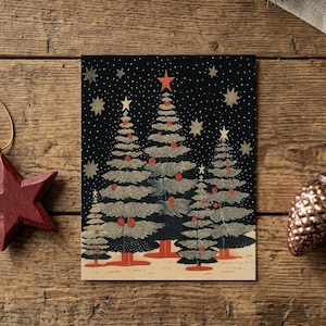 May include: A rectangular greeting card featuring a graphic illustration of four stylized Christmas trees in shades of dark green and cream against a black starry sky, accented with red ornaments and a red star topper, flanked by a red star and pinecone.