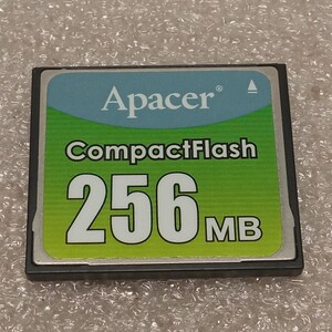 May include: A CompactFlash memory card featuring the Apacer logo. The card has a green and blue label with the text "CompactFlash" and "256MB" in large white letters. The card is rectangular with a black border.