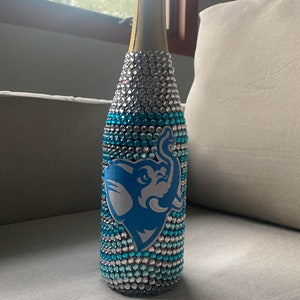May include: A champagne bottle decorated with blue and silver rhinestones, featuring a blue elephant logo.