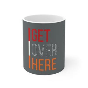 May include: A gray ceramic mug with the text "GET OVER HERE" in red and orange letters. The letters are stylized with a white outline.