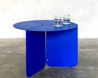 Op de afbeelding: Een ronde, blauwe, opvouwbare bijzettafel met drie poten. De tafel is gemaakt van metaal en heeft een glad, modern ontwerp.