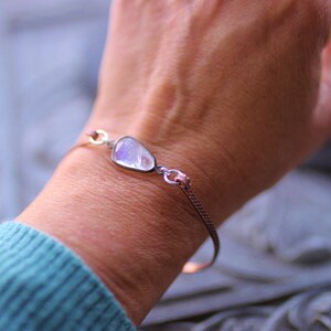 May include: A silver bracelet with a large, iridescent moonstone charm. The bracelet is on a person's wrist.