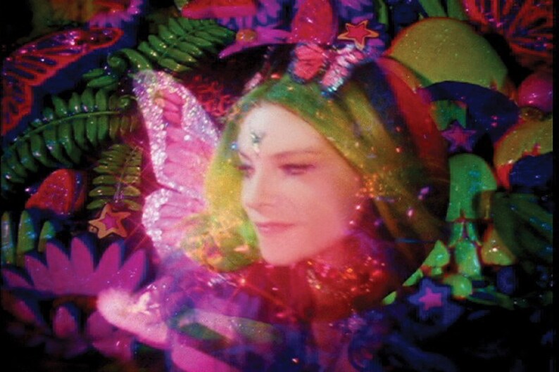 May include: A woman with green hair and a sparkly butterfly headband is surrounded by colorful, glittery decorations. The decorations include stars, butterflies, and leaves. The woman is smiling and looking to the side.