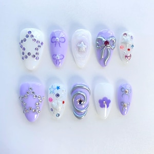 May include: Set of ten purple and white false nails with various designs, including stars, bows, and glitter.