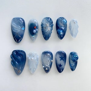 Könnte beinhalten: Zehn blaue und weiße Nageldesigns mit verschiedenen Mustern und Verzierungen, darunter Sterne, Wirbel und Glitzer.
