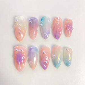 Könnte beinhalten: Zehn pastellfarbene Kunstnägel mit Perlenakzenten. Die Nägel sind mit einem Farbverlauf in Rosa, Lila und Blau verziert.
