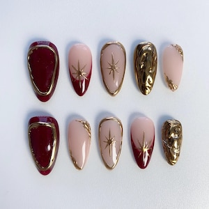 Puede incluir: Conjunto de diez uñas postizas con un diseño burdeos y dorado. Algunas uñas presentan una estrella dorada, otras tienen un diseño dorado y algunas son burdeos con un contorno dorado.