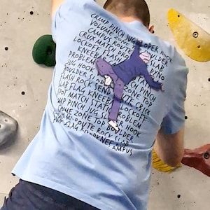 Könnte beinhalten: Ein hellblaues T-Shirt mit einer Grafik einer Person, die eine Wand klettert. Der Text auf dem T-Shirt listet verschiedene Kletterbegriffe auf, darunter "Crimp Pinch", "Volume Zone", "Campus Route", "Crux Match", "Lockoff Flash", "Kneebar", "Problem", "Jug Hook", "Boulder Send", "Flash Rock Send", "Slab", "Dyno", "Tatt", "One Top", "Criex", "Ch Pinch", "Pot Match Static", "Problem", "Whip Pinch", "Jug", "Slider Hook", "Caue Zone", "Top Boulder", "M. Doute", "Rocky Slab", "Flag", "K-D", "Nef", "Ampus".