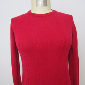 Puede incluir: Un suéter rojo de manga larga con un patrón de punto de cable.