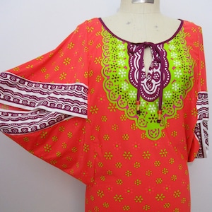 May include: A bright orange tunic with a green, white, and purple patterned neckline. The tunic has a wide, flowing sleeve with a white and purple trim.