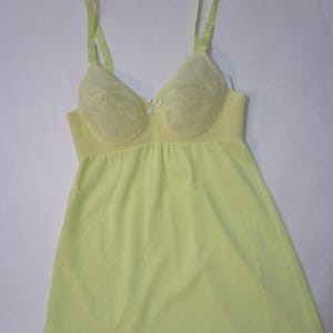 May include: A light yellow slip with a lace trim and built-in bra. The bra has a lace design and a bow in the center.