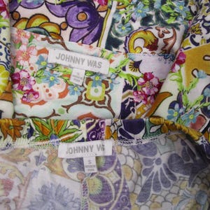 Puede incluir: Una prenda de la marca Johnny Was con un vibrante estampado floral y de cachemira multicolor en tonos morado, verde, amarillo y rosa. La etiqueta de tela blanca muestra el texto JOHNNY WAS y la talla S, indicando que fue hecha en Per&uacute;.