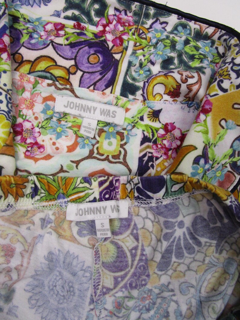 Puede incluir: Una prenda de la marca Johnny Was con un vibrante estampado floral y de cachemira multicolor en tonos morado, verde, amarillo y rosa. La etiqueta de tela blanca muestra el texto JOHNNY WAS y la talla S, indicando que fue hecha en Per&uacute;.