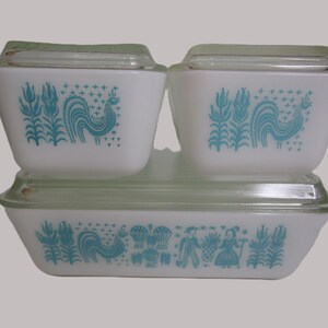 Op de afbeelding: Drie witte melkglazen voorraadbakjes met doorzichtige glazen deksels. Twee kleinere vierkante schaaltjes en een grotere rechthoekige schaal zijn voorzien van een turquoise blauw patroon van hanen, maïskolven en een paar in klederdracht.