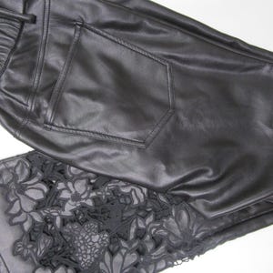 Pu&ograve; includere: Pantaloni neri con finitura liscia e una tasca posteriore. La parte inferiore della gamba presenta un intricato motivo floreale in pizzo nero intagliato che si estende sul tessuto, creando un contrasto dettagliato con il materiale nero solido.